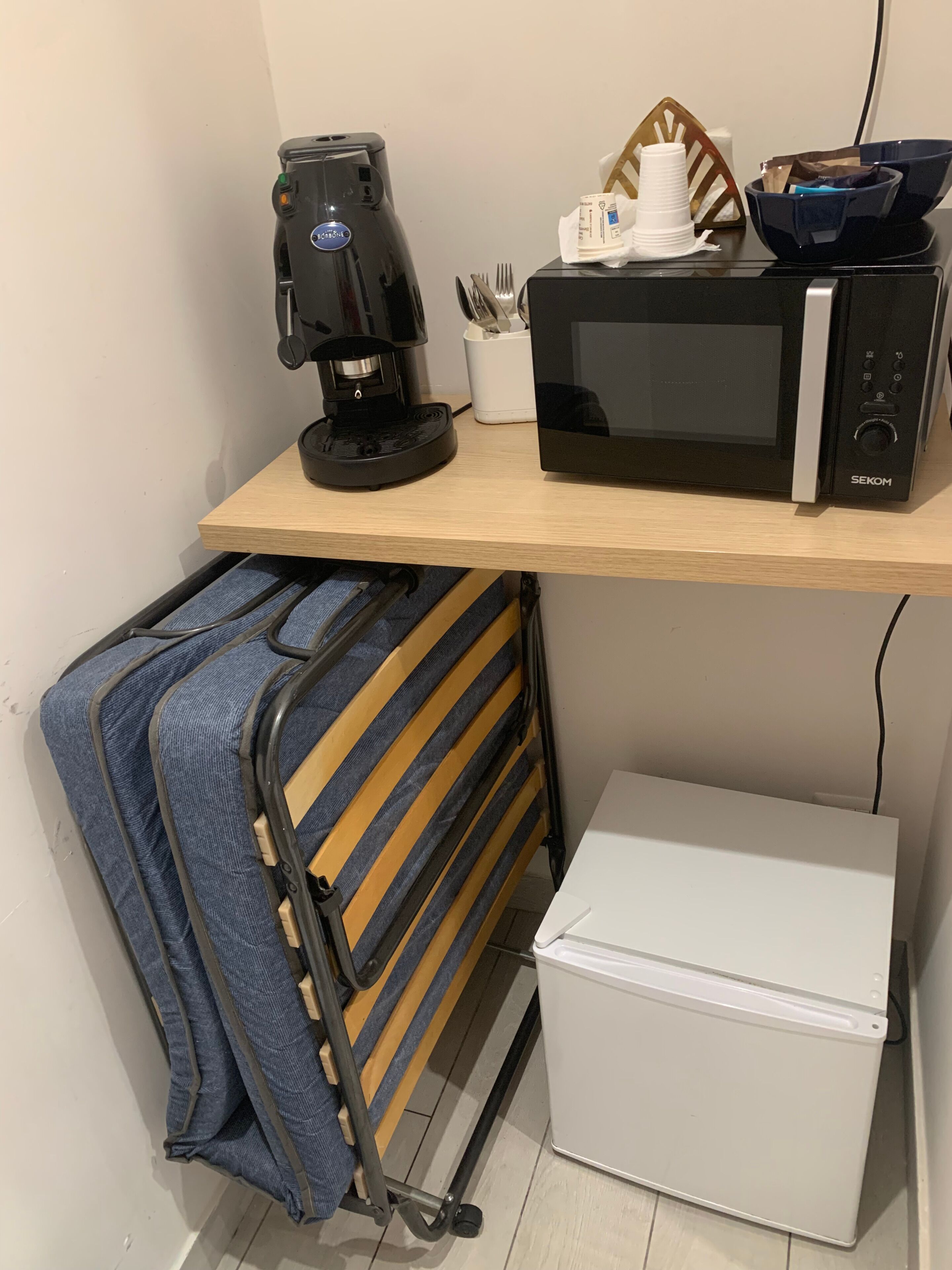 Un angolo cottura con macchina del caffè, forno a microonde e contenitori per alimenti.