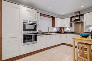 Eine moderne Küche mit weißen Schränken, Edelstahlgeräten und einem Holztisch.