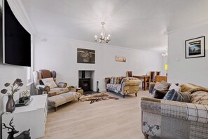 A spacious living room with a fireplace, comfortable seating, and a chandelier. - Glenmore Lodge | Luxury Braemar Highland Retreat | Walk to Village | Sleeps 6 (Braemar)