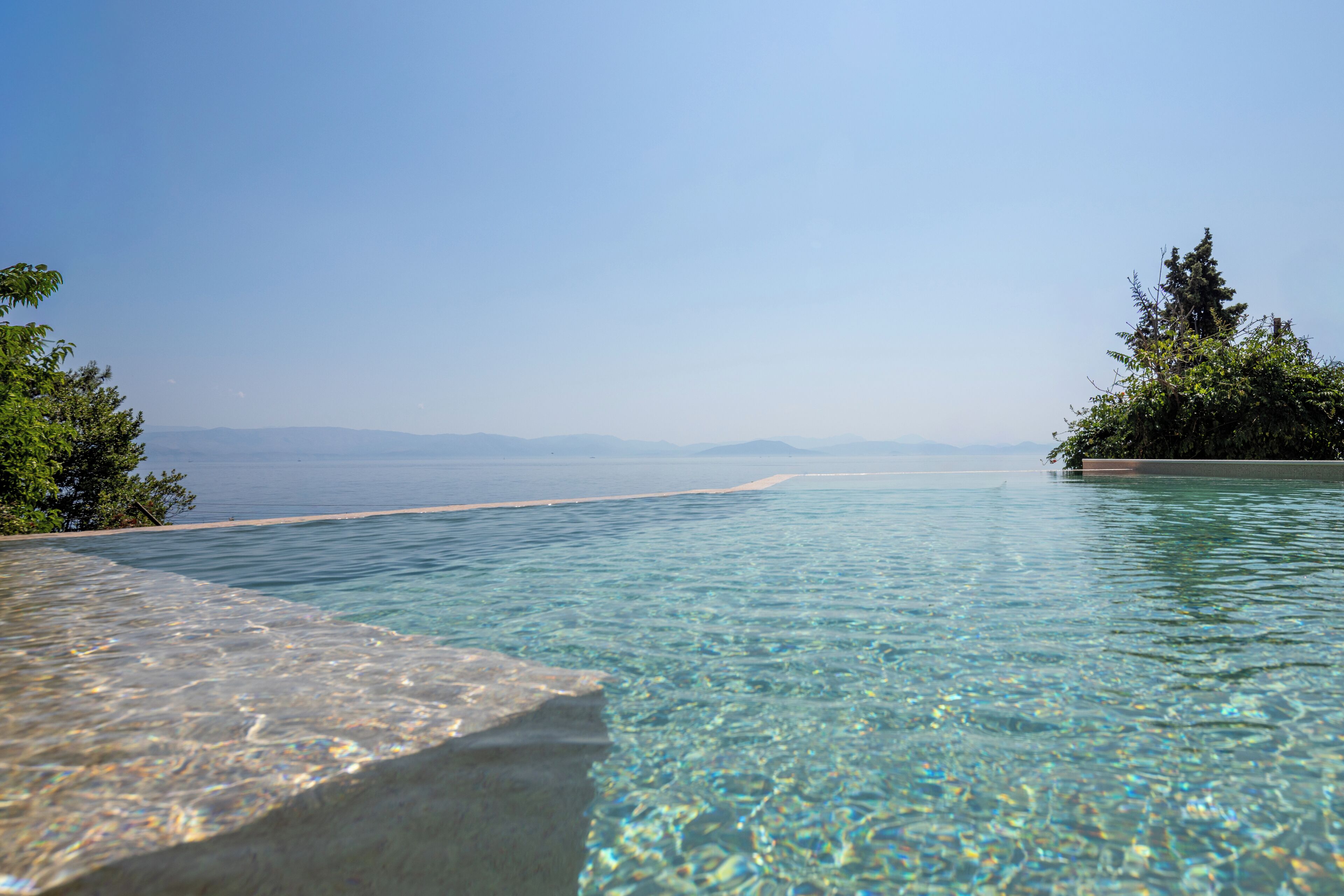 Une magnifique piscine à débordement, avec vue sur la mer et les montagnes lointaines.