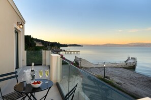 A balcony with a table, a bottle of champagne, and glasses, overlooking a calm sea and a pier. - Luxury Beachfront Achillion Bay Villa | Infinity Pool & Breathtaking Sea Views (Mpenitses)
