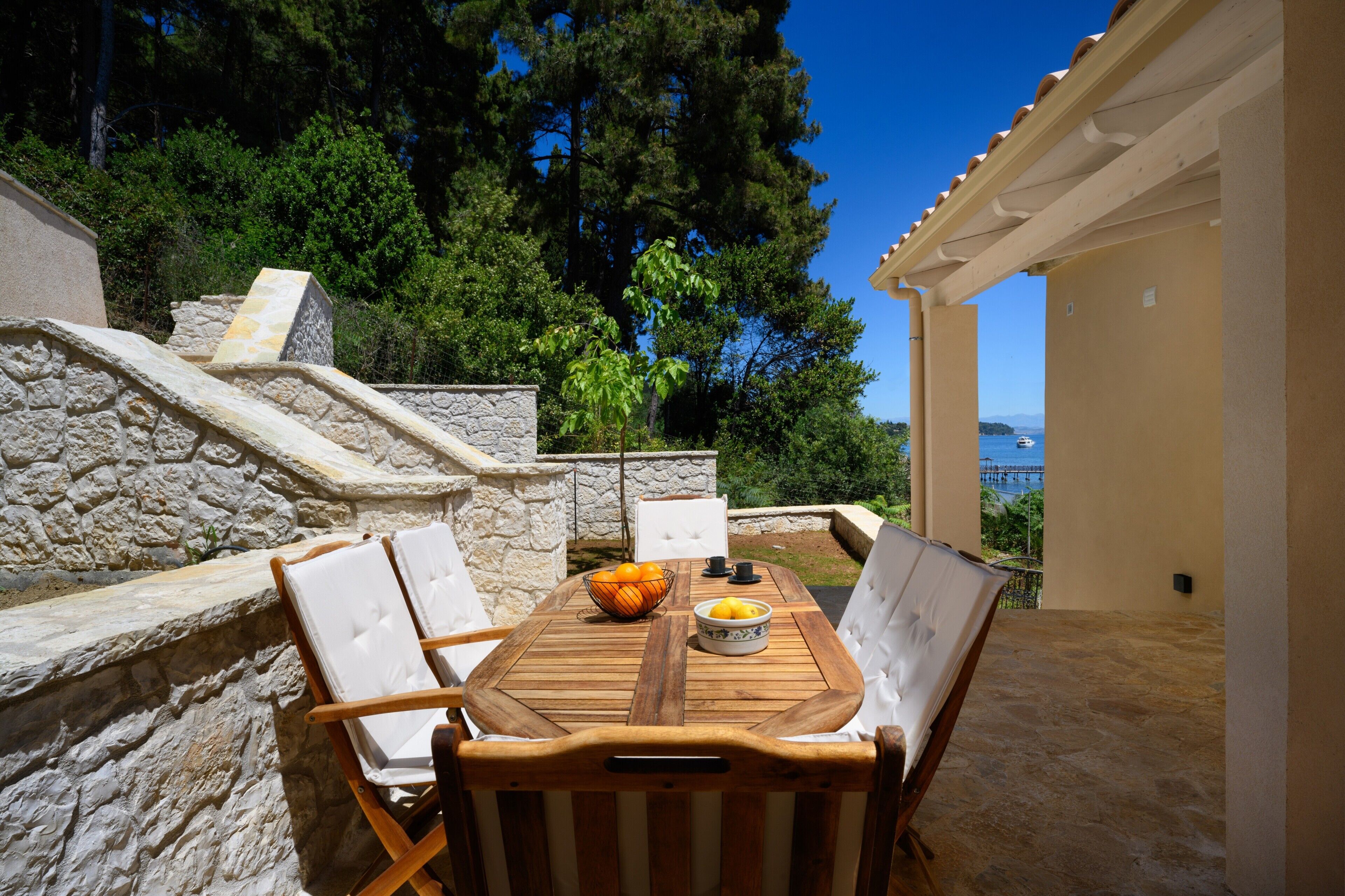 A stone wall, a wooden table with chairs, and a view of the sea.