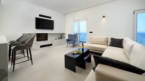 Una sala de estar moderna con un televisor de pantalla plana, un sofá, una mesa de centro y una zona de comedor con taburetes de bar.
