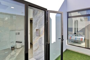 Habitació d'hotel moderna amb una porta de vidre que dona a un bany, un llit amb un edredó de colors i vistes a l'exterior.