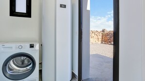 A laundry area with a front-loading washing machine, a tall white appliance, and a door leading to an outdoor area with a stone wall.