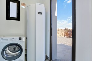 Un espace buanderie comprenant un lave-linge à chargement frontal, un appareil électroménager blanc de grande taille, et une porte donnant sur un espace extérieur avec un mur en pierre.