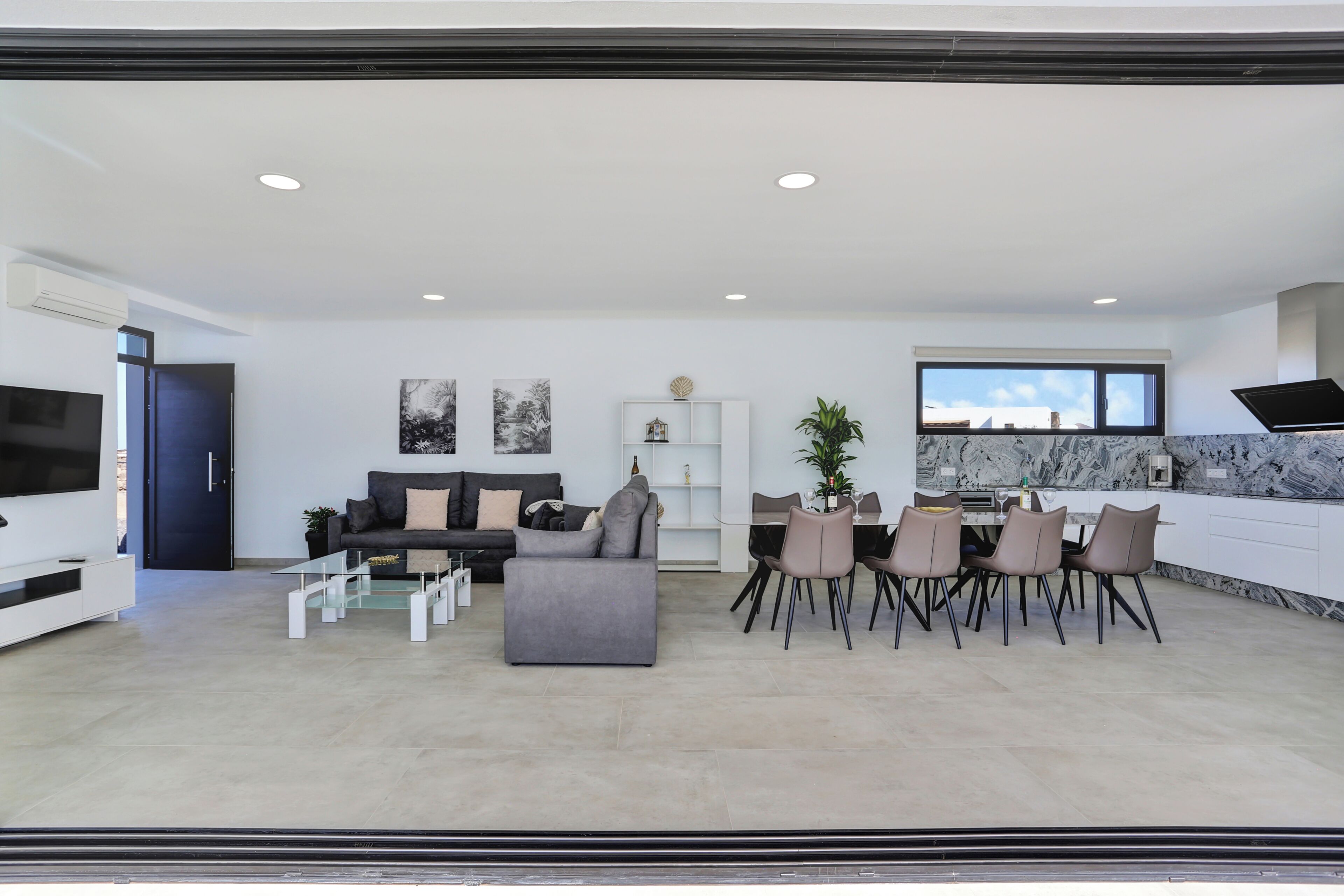 A modern living room with a sofa, coffee table, TV, and dining area with chairs and a table.