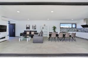 Een moderne woonkamer met een bank, salontafel, televisie en een eethoek met stoelen en een tafel.