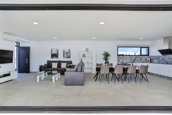Un salon moderne comprenant un canapé, une table basse, un téléviseur et un coin repas avec des chaises et une table.