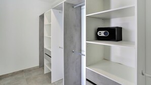 A walk-in closet with open doors, revealing multiple shelves and a black safe on the top shelf.