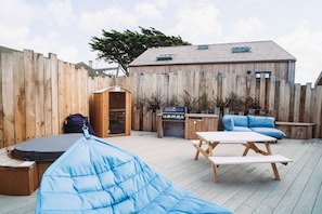 An outdoor patio with a wooden deck, a barbecue grill, a wooden shed, and blue cushioned seating.