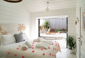 A bedroom with a bed, pillows, a towel, and a view of an outdoor patio with plants.