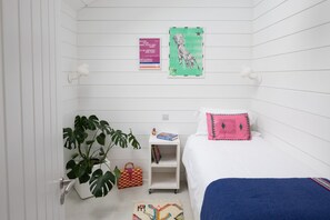 A bedroom with a bed, a bedside table, a nightstand, a potted plant, and a wall with two posters.