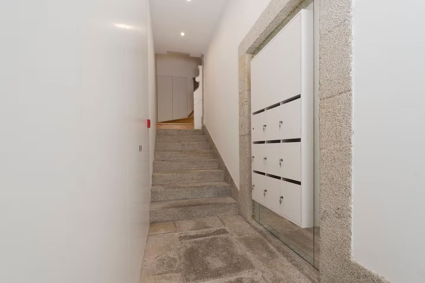 Un estrecho pasillo con una escalera de piedra que lleva a una puerta con varios casilleros.