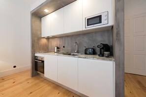 A compact kitchen with white cabinets, a microwave, a toaster, a coffee maker, and a sink. - Rico's Apartment 2D - Perfectly Located in Central Porto (Porto)