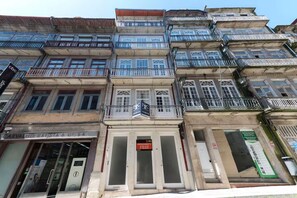 A multi-story building with balconies, a storefront with a sign, and a door with a sign above it. - Rico's Apartment 2D - Perfectly Located in Central Porto (Porto)