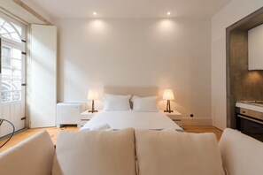 A modern hotel room with a large bed, two bedside lamps, a wooden floor, and a view of the city through a large window. - Rico's Apartment 2D - Perfectly Located in Central Porto (Porto)