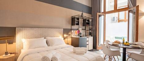 A hotel room with a large bed, a desk, a chair, and a dining table.