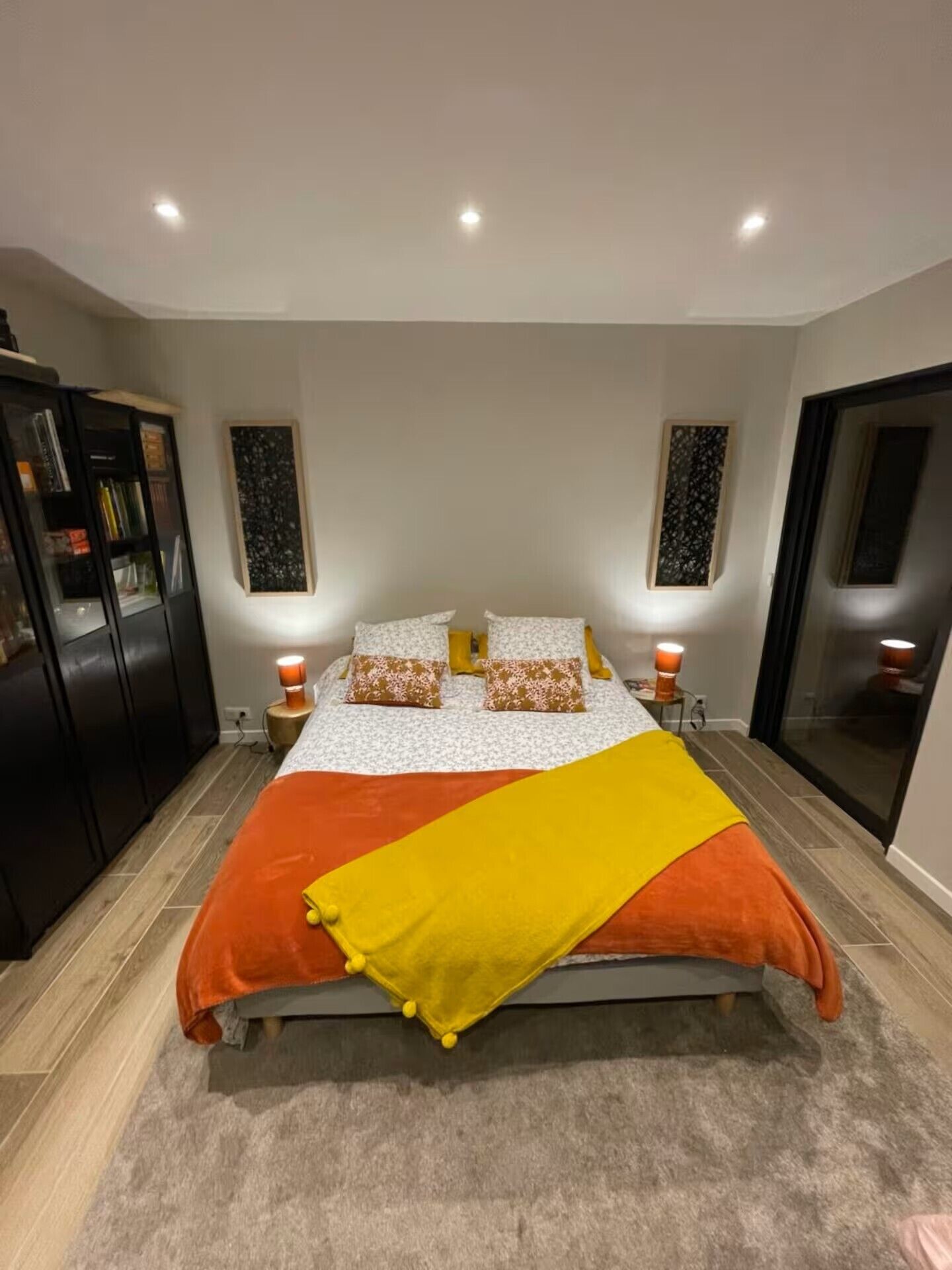 A bedroom with a bed, two bedside lamps, a nightstand, a wardrobe, and a large window.