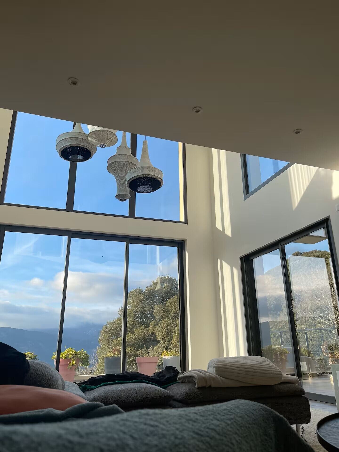 A modern bedroom with large windows, a view of the outdoors, and a unique ceiling light fixture.