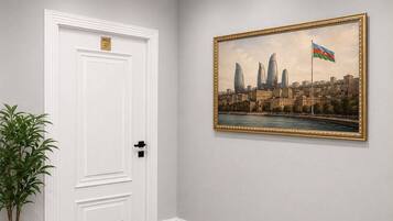 A hallway with a white door, a framed cityscape painting, and a potted plant.