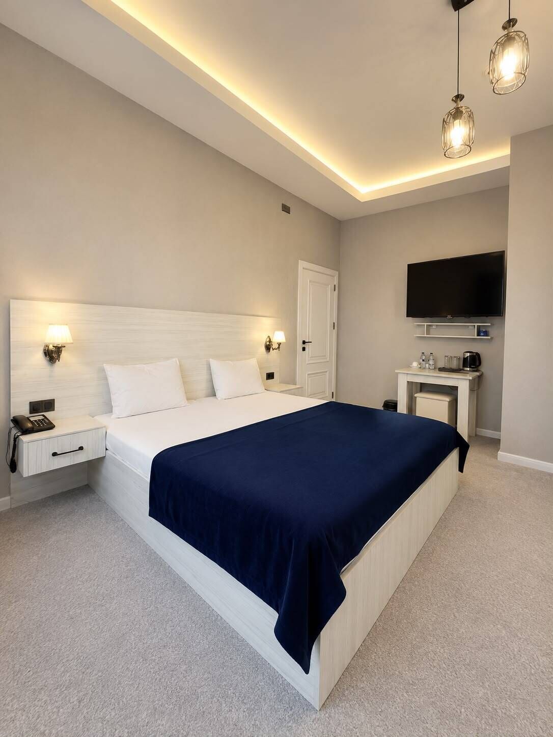 A modern bedroom with a large bed, bedside lamps, a flat-screen TV, and a desk with a coffee maker.