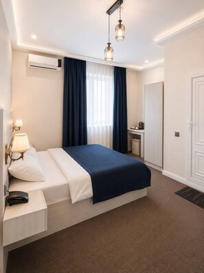 A hotel room with a bed, bedside table, lamp, air conditioning unit, and a desk with a chair. - Central Way Baku (Baku)