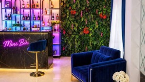 A bar area with a neon sign, a blue sofa, and magazines on a table. - Central Way Baku (Baku)