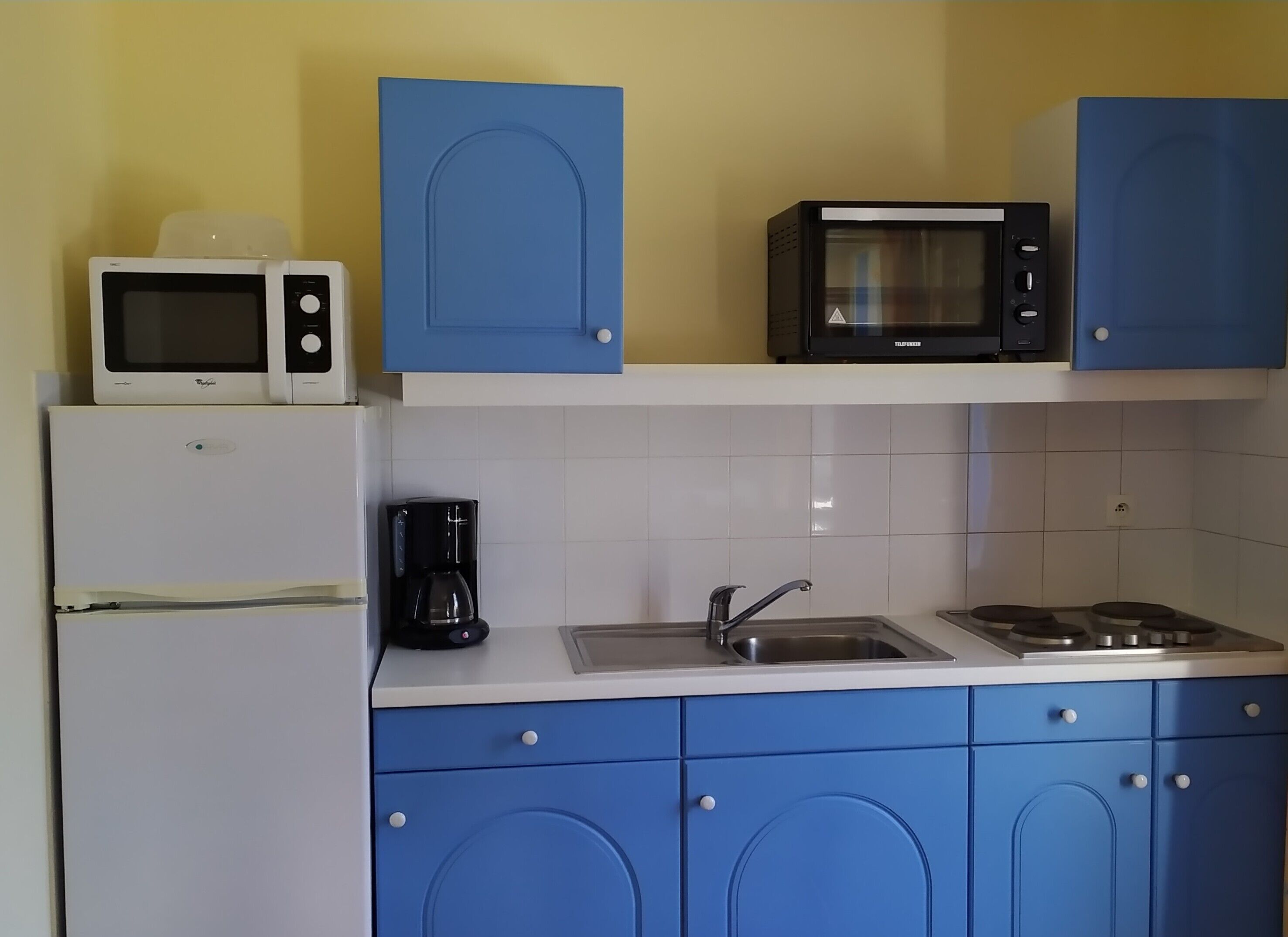 A kitchen with a refrigerator, microwave, coffee maker, sink, and stove.