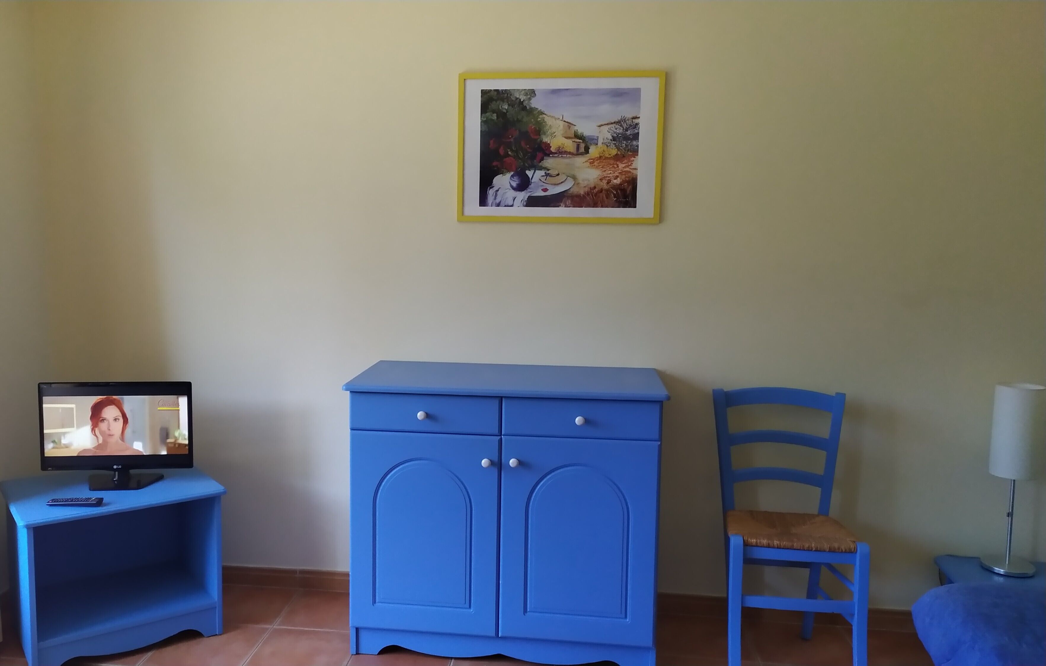 A room with a blue cabinet, a chair, a desk with a computer, and a framed picture on the wall.