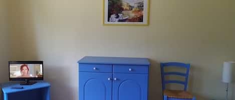 A room with a blue cabinet, a chair, a desk with a computer, and a framed picture on the wall.
