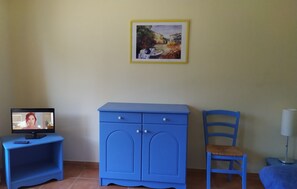 Una habitación con un armario azul, una silla, un escritorio con una computadora y un cuadro en la pared.