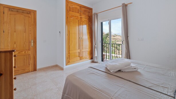 Ein Schlafzimmer mit einem Bett, einem Holzschrank und einer Glastür zum Balkon.
