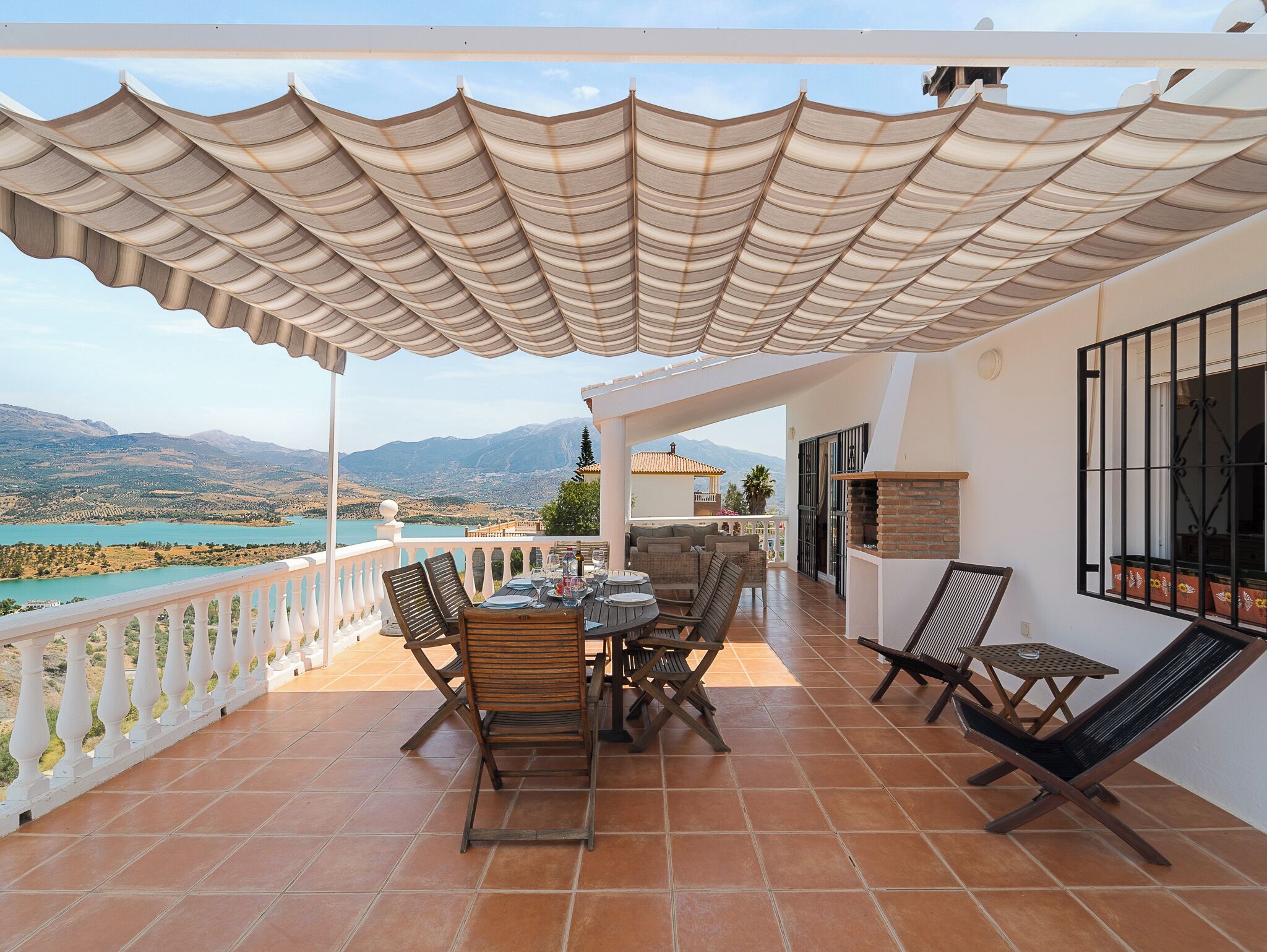 Eine Terrasse mit Tisch und Stühlen, Blick auf das Meer und ein Berg im Hintergrund.