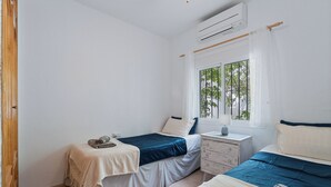 Ein Schlafzimmer mit zwei Betten, einem Fenster mit Blick auf Bäume und einer Klimaanlage.