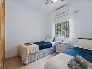 A bedroom with two beds, a window with a view of trees, and an air conditioning unit. - Casa Juan for 8 people, with a private pool, a patio with a grill, and a magnificent lake view (Viñuela)