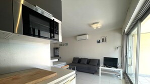 A modern kitchen with a dishwasher, a wooden countertop, and a grey sofa in the living area. - 1-BR Villa with Terrace and Air Conditioning - Cap d'Agde (Cap d'Agde)