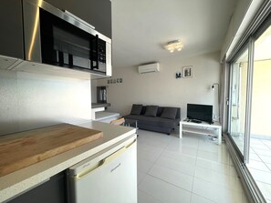 A modern kitchen with a dishwasher, a wooden countertop, and a grey sofa in the living area. - 1-BR Villa with Terrace and Air Conditioning - Cap d'Agde (Cap d'Agde)