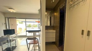 A modern hotel room with a TV, a dining area with a table and chairs, a kitchen area, and a view of the outside. - 1-BR Villa with Terrace and Air Conditioning - Cap d'Agde (Cap d'Agde)
