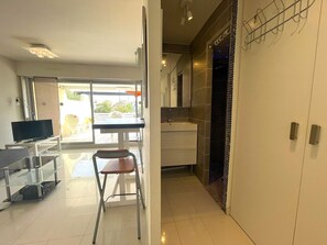 A modern hotel room with a TV, a dining area with a table and chairs, a kitchen area, and a view of the outside. - 1-BR Villa with Terrace and Air Conditioning - Cap d'Agde (Cap d'Agde)