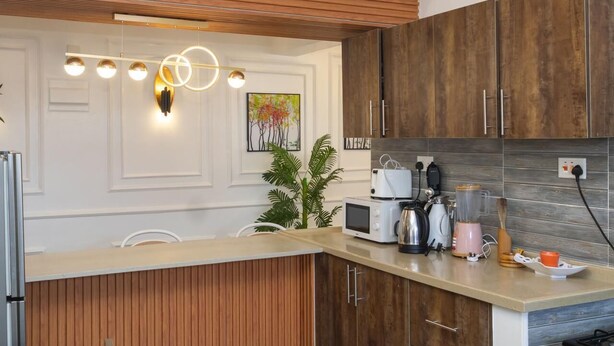 Une cuisine moderne avec des meubles en bois, un four à micro-ondes encastré, une machine à café et une plante.