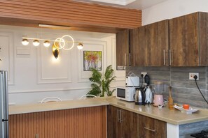 A modern kitchen with wooden cabinets, a built-in microwave, a coffee maker, and a plant. - Luxury 2-Bedroom Apartment in Nyali with Pool & Beach Access in Mombasa (Mombasa)