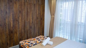 Une chambre d’hôtel avec un lit, une couvre-lit à motifs, une armoire en bois et une fenêtre ornée de rideaux légers.