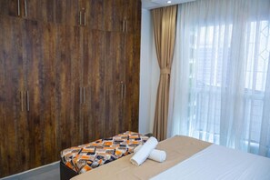 A hotel room with a bed, a patterned bedspread, a wooden wardrobe, and a window with sheer curtains. - Luxury 2-Bedroom Apartment in Nyali with Pool & Beach Access in Mombasa (Mombasa)
