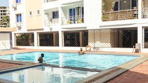 Une piscine où se trouvent deux personnes, entourée d’un bâtiment doté de balcons et de grandes fenêtres.