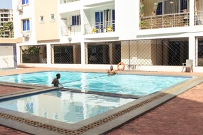 A swimming pool with two people in the water, surrounded by a building with balconies and large windows. - Luxury 2-Bedroom Apartment in Nyali with Pool & Beach Access in Mombasa (Mombasa)