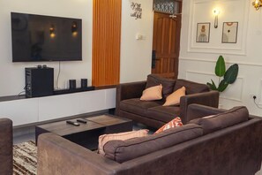 A modern living room with a flat-screen TV, a dark brown sofa set, a coffee table, and a plant. - Luxury 2-Bedroom Apartment in Nyali with Pool & Beach Access in Mombasa (Mombasa)