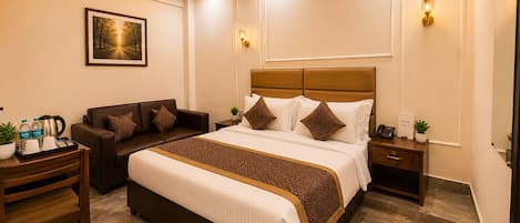 Habitación de hotel con una cama grande, un sofá, un escritorio con una bandeja de artículos de cortesía y un ventilador de techo.