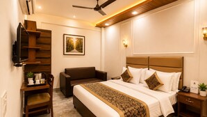 Ein Hotelzimmer mit Bett, Schreibtisch, Sessel, Fernseher und Deckenventilator.