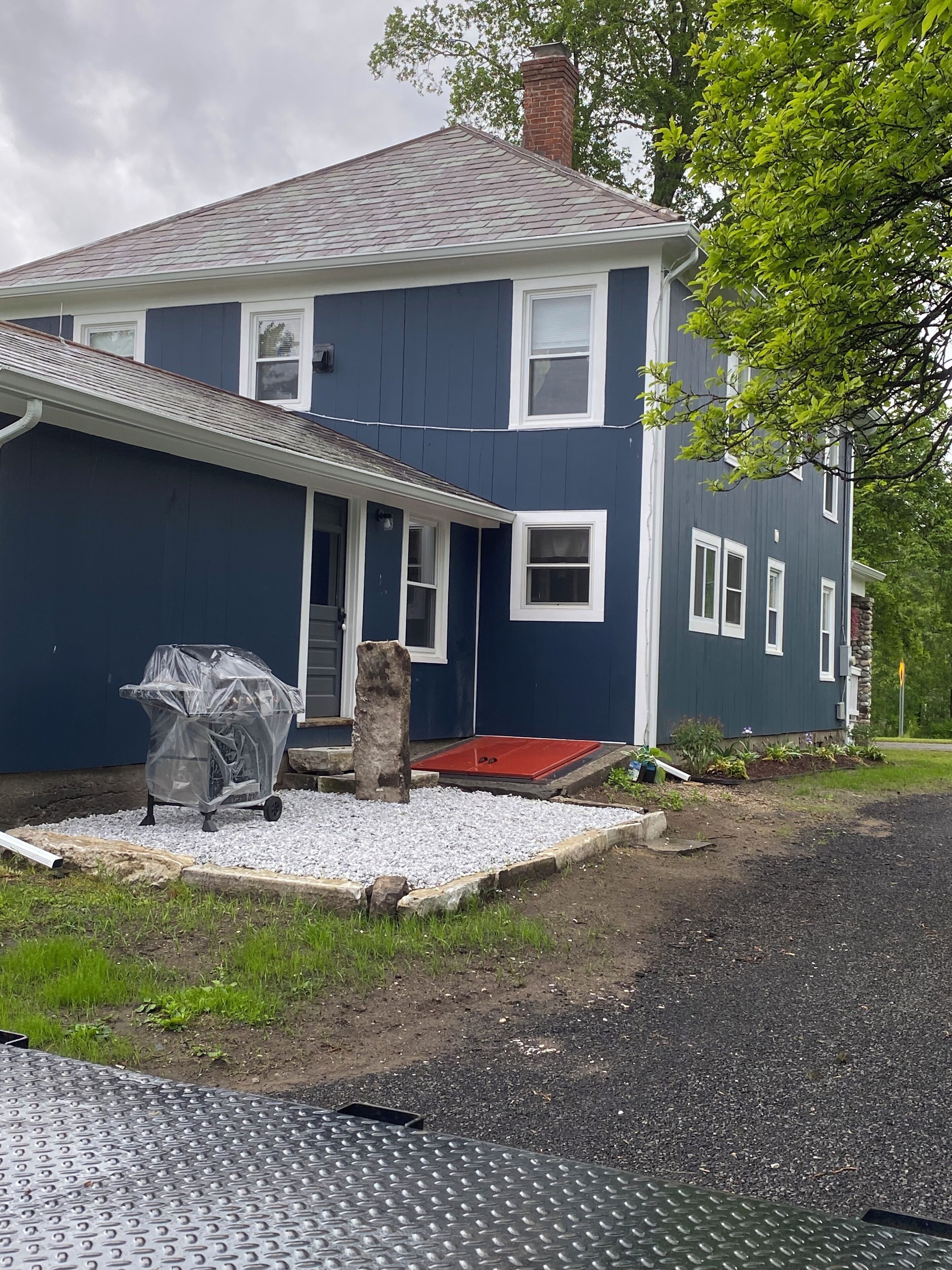 Une maison à deux étages avec une porte d’entrée rouge, un barbecue couvert et une allée gravillonnée.